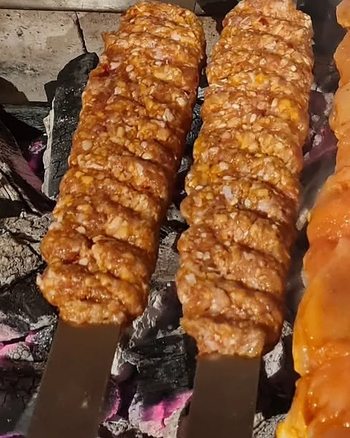 Zwei rohe Adana-Spieße über glühender Holzkohle
